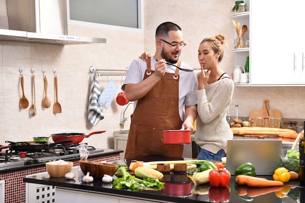 Loving young Asian couple cooking in kitchen making healthy food together feeling fun