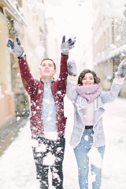 愛する若いカップルは雪で遊んで、朝の冬の街を歩く