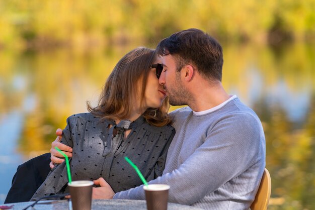 Amare la giovane coppia baci e coccole in un ristorante all'aperto che si affaccia su un lago