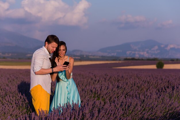 Loving young couple in lavender field having fun with smartphone