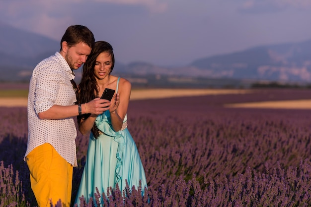 любящая молодая пара в лавандовом поле развлекается со смартфоном