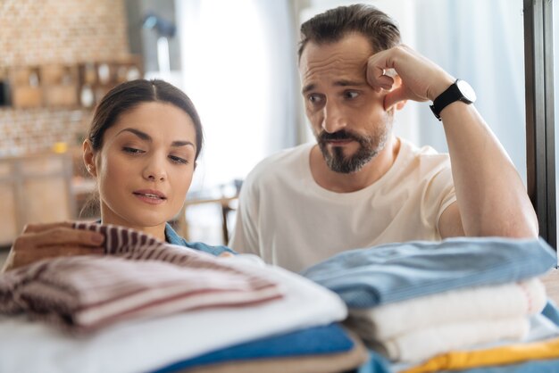 Loving young couple posing near clothes while bearded husband leaning on hand and staring at his wife