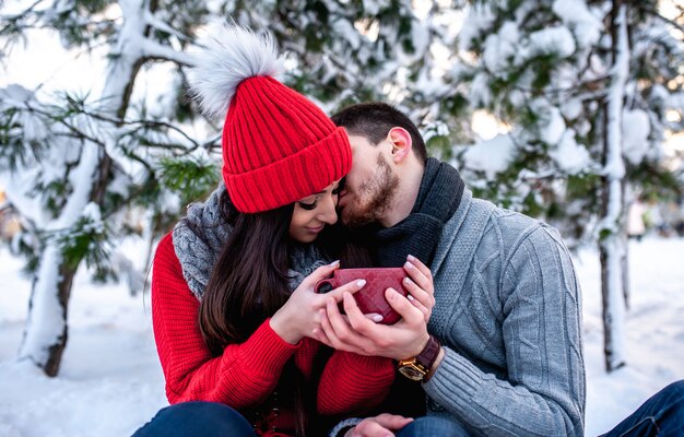 雪に覆われた森で休んで若いカップルを愛する。ハグとキス。休暇の概念