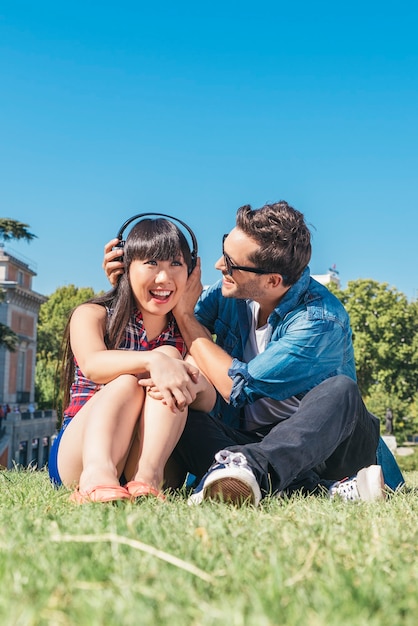 Loving young couple in summer park listening music with headphones