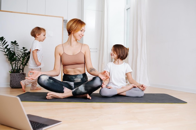 Loving young mom doing yoga with her daughter At the kitchen at home