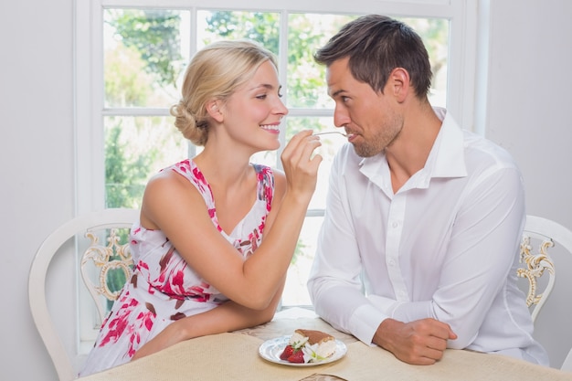 Loving young woman feeding man pastry at home