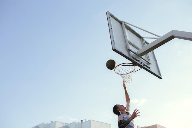 Low angle of basketball player jumping and throwing ball into hoop while playing street ball