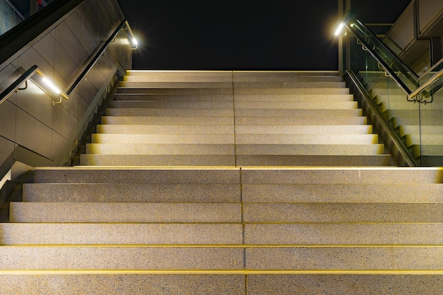 Low angle closeup of stairs with yellow lining and metallic rails with lights at night