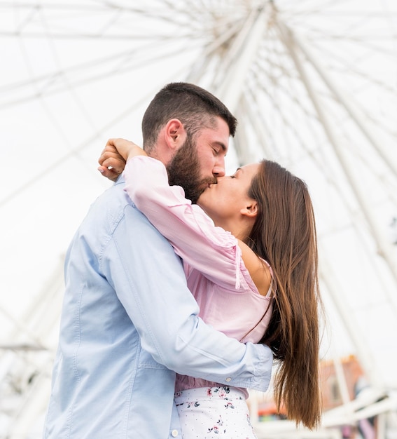 Low angle of couple kissing in front of big wheel