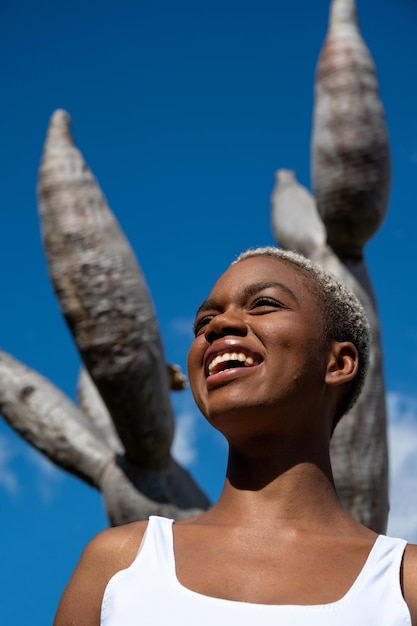 Low angle of delighte black female with short hair laughing and looking away in front of dragon tree