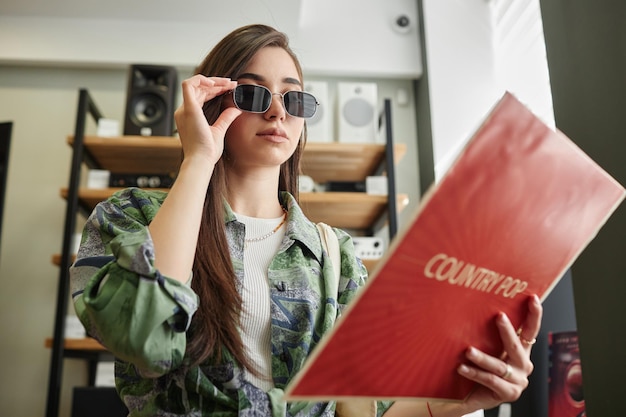 音楽店でヴィニールレコードを握っている低角度のファンキーな若い女性