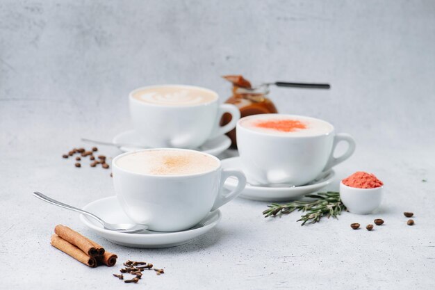 Low angle image of cappuccino with cream and spices in three\
cups on saucers