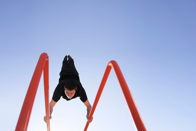 Foto basso angolo di un uomo che fa la verticale in piedi sulla barra, in un parco con bilanciere. esercizio all'aperto. concetto di vita sana, sport, allenamento, ginnastica ritmica.