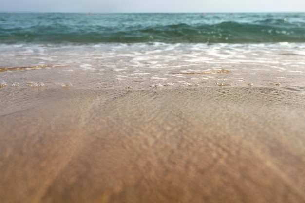 地上からの低角度の写真 – 海から濡れた浜辺の砂、空気中の水滴、小さな波、遠くにぼやけた海。抽象的な休暇の背景。