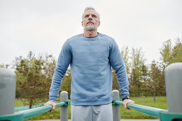 Low angle portrait of active mature man exercising on parallel bars outdoors copy space