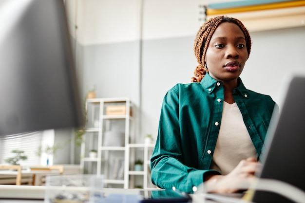 Low angle portrait of black young woman using laptop while working at desk in software development o