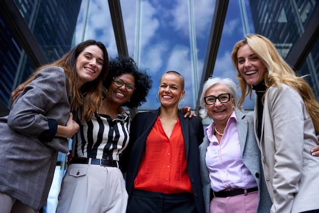 Low angle portrait business women hugging together outside office happy looking laughing at camera