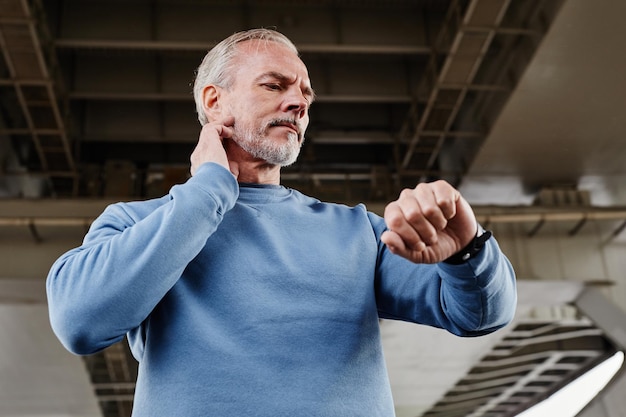 Low angle portrait of handsome mature man tracing pulse rate with smartwatch during outdoor workout