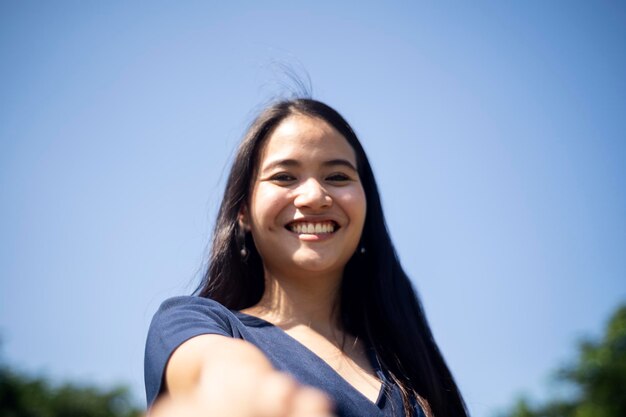 Low angle portrait of smiling young woman against clear blue sky