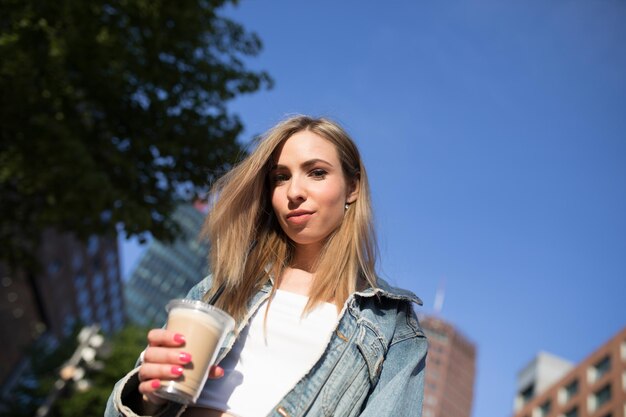 都市で使い捨てカップを握っている女性の低角度の肖像画