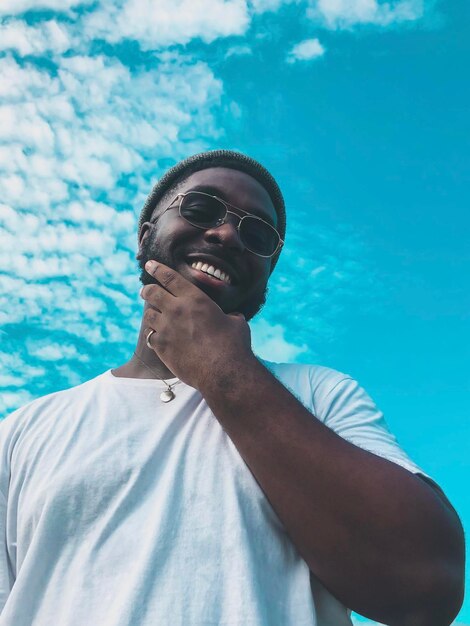 Low angle portrait of young man standing against blue sky