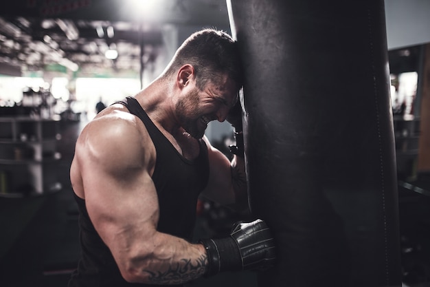 Low angle portrait of young tired sports man leaning on punching bag