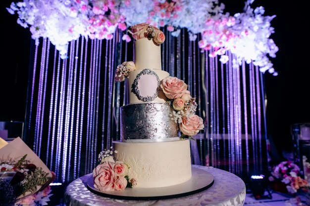 Low angle shoot of elegance Wedding cake decorated with flowers and ribbons on the table Evening decoration and colour lights