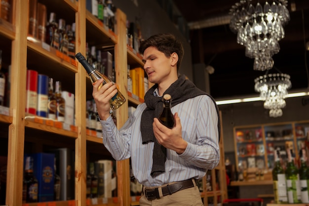 Low angle shot of a handsome young elegant man choosing wine to buy at the supermarket