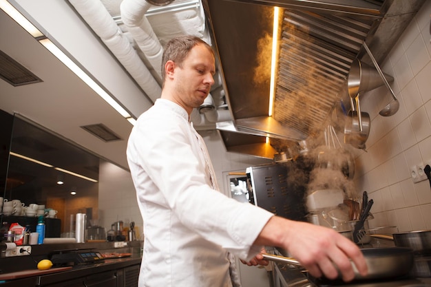 low angle shot of a male chef using stove, cooking at restaurant kitchen