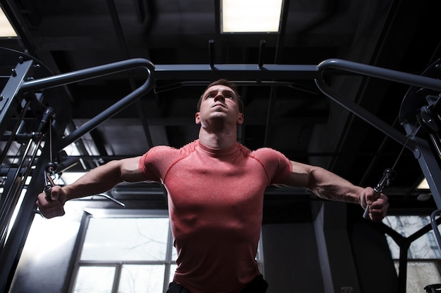 Low angle shot of a muscular bodybuilder working out in cable crossover gym machine