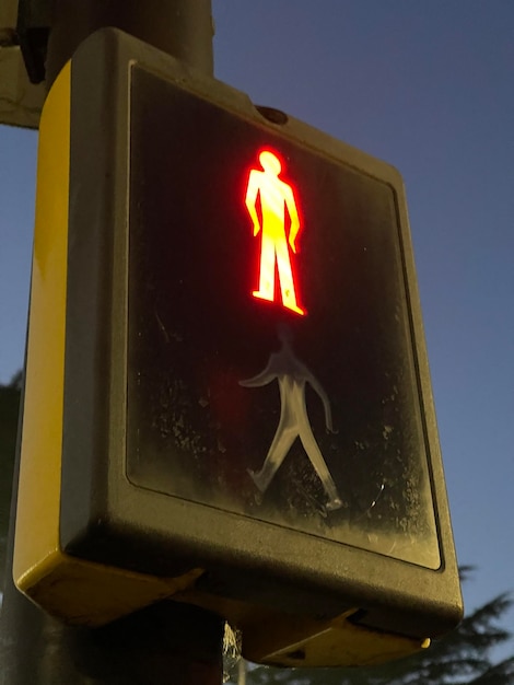 Low angle shot of pedestrian lights glowing red against evening sky