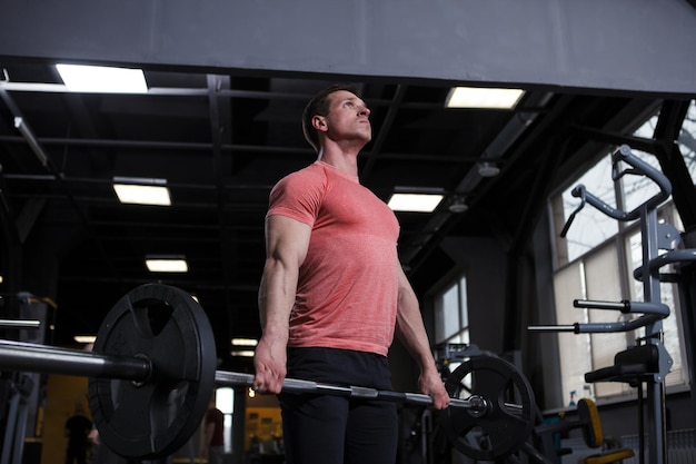 Low angle shot of a ripped strong sportsman holding heavy barbell