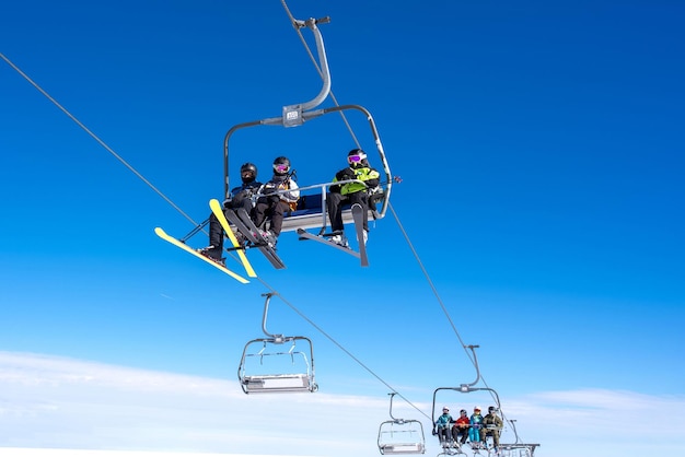 A low angle shot of skiers on a ski lift at a mountain resort with the sky and mountains in the background