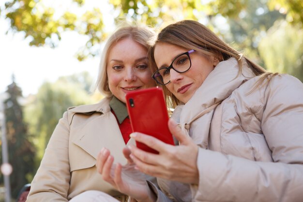 Low angle shot of two mature women using smart phone in the park