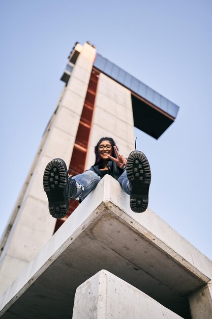 Photo low angle shot of young brunette latina woman wearing glasses fur jacket and big boots sitting with