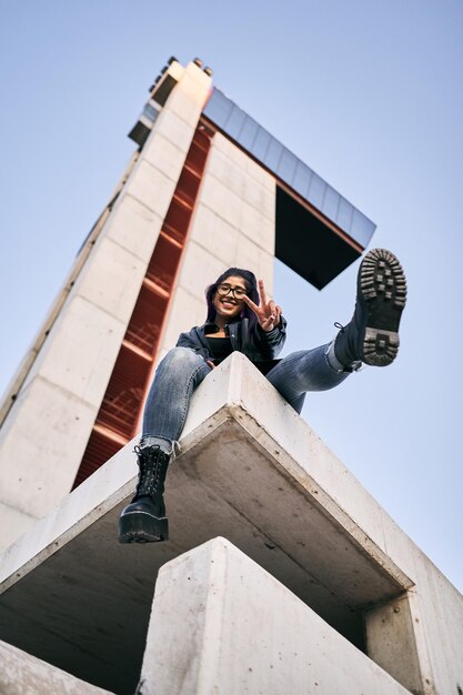 Photo low angle shot of young latin woman wearing glasses fur jacket and big boots doing v for victory