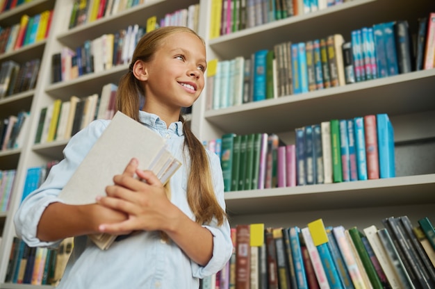 Angolo basso di un bellissimo scolaro sorridente con una pila di libri che guarda in lontananza