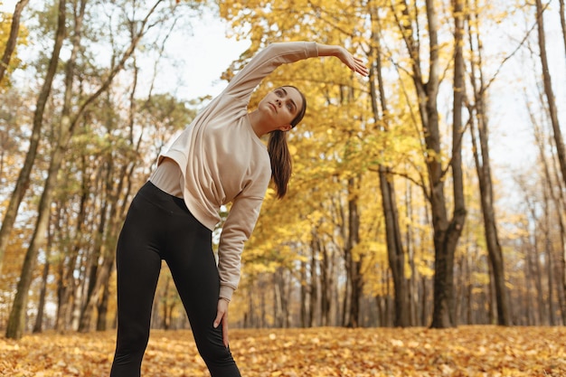 Low angle of sportswoman doing side bend while training during fitness workout in autumn in forest