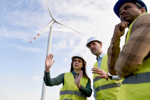 Low angle of team of caucasian and latin engineers standing on wind turbine field and discussing