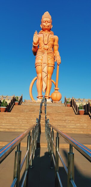 Low angle view of 108 feet tall statue of lord hanuman on building against clear blue sky