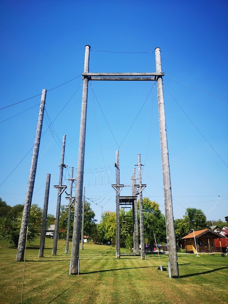 Low angle view of adrenalin park on field against clear blue sky