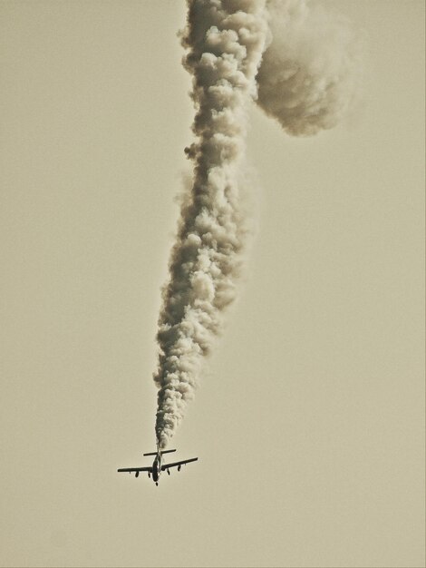 Photo low angle view of airplane emitting smoke in clear sky