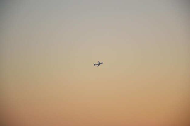 Low angle view of airplane flying against clear sky during sunset