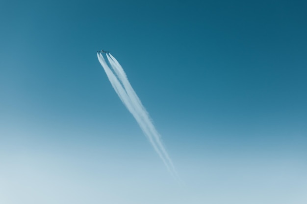 澄んだ青い空で蒸気の痕跡で飛ぶ飛行機の低角度の景色