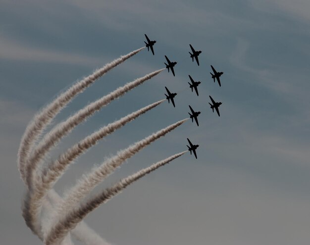 Photo low angle view of airplanes with trails in flight