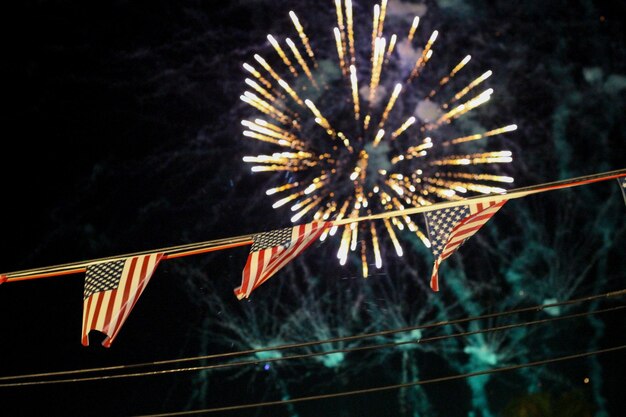 Foto vista a bassa angolazione delle bandiere americane contro i fuochi d'artificio illuminati di notte