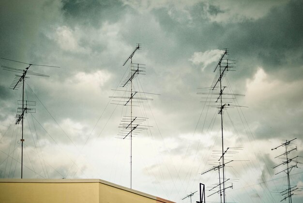 Low angle view of antennas against cloudy sky