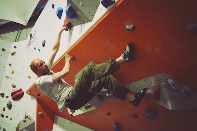 Foto vista ad angolo basso di un atleta che si arrampica su una parete rocciosa in palestra