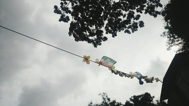 Low angle view of balloons hanging from dahi handi by trees against sky