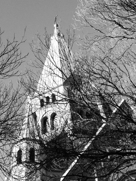 Photo low angle view of bare trees by church against clear sky